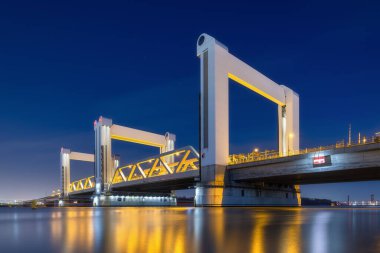 Botlek Köprüsü, Rotterdam, Hollanda. Geceleri köprünün manzarası. Arabalar ve demiryolu taşımacılığı. Mimari peyzaj. Suyun yüzeyindeki yansımalar..