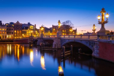 Mavi köprü, Amsterdam, Hollanda. Blauwbrug. Akşam manzarası. Mavi gökyüzü ve şehir ışıkları. Hollanda kanalları. Suyun yüzeyindeki yansımalar. Tasarım ve duvar kağıdı fotoğrafçılığı.