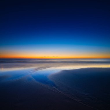 Gün batımında deniz manzarası. Deniz kıyısındaki kum hatları. Gün batımında parlak gökyüzü. Dalgalar alçaldığında kumlu bir sahil. Duvar kağıdı ve arkaplan.