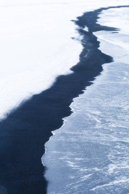 Deniz kıyısında. Fırtınalı deniz manzarası, siyah volkanik kum ve kar. İzlanda 'da manzara. Kış manzarası. Soyut doğal manzara.