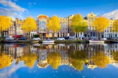 Sonbaharda Amsterdam 'da. Hollanda 'nın başkenti. Eski evler ve kanal manzarası. Suyun yüzeyindeki yansıma. Ağaçlarda sarı yapraklar. Kartpostal, arkaplan veya duvar kağıdı.