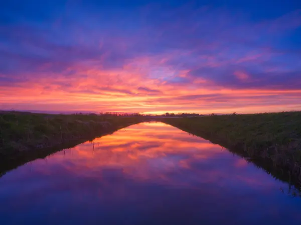 Nature. The river during a bright sunset. Bright sky with clouds during sunset. Landscape in the summertime. Reflections on the surface of the water.