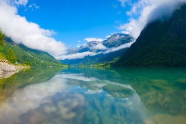 Beautiful mountain lake in Norway. Nature in fjords. High mountains and reflections on the surface of the water. Clouds over the rocks. Vacation and travel in summer Norway. clipart