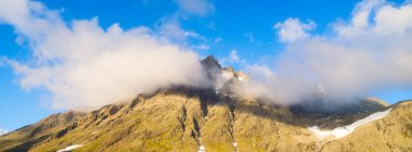 Dağ manzarası. Vadideki yüksek bir dağın manzarası. Kocaman keskin kayalar ve bulutlar. Yaz mevsiminde manzara. Kaya tırmanışı ve yürüyüş için bir yer..