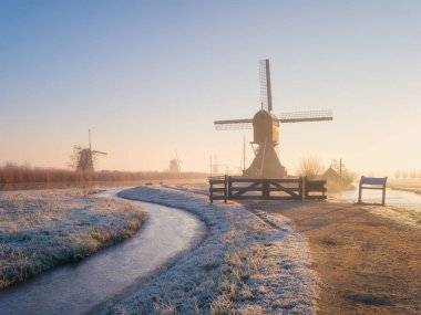 Hollanda 'da güneş doğarken yel değirmenleri. Sisli bir sabah ve güneş ışığı. Hollanda kanalları. Panoramik doğal manzara. Arkaplan, duvar kağıdı, kartpostallar için fotoğraf.