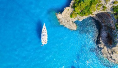 Deniz kıyısı ve yatın insansız hava aracı görüntüsü. Kaya kıyısı ve deniz suyu. Tatil ve seyahat. Yaz deniz manzarası. Hava görüntüsü. Şeffaf deniz suyu ve dalgalar. Arkaplan, kartpostallar, duvar kağıtları.