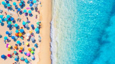 Yaz tatili ve dinlenme. Plaj, insanlar ve şemsiyeler. Kumsaldaki İHA 'nın ve gök mavisi denizin üst görüntüsü. İHA 'dan sahile bak. Arkaplan, duvar kağıdı, kartpostallar.