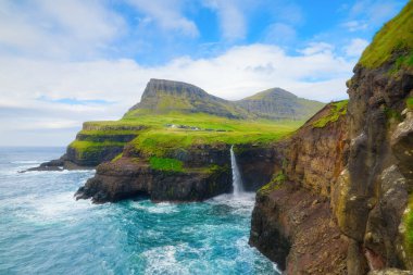 Mulafossur Şelalesi, Faroe Adaları, Danimarka. Seyahat için güzel bir yer. Şelalenin, deniz koyunun ve dağların panoramik manzarası. Duvar kağıdı, arkaplan, kartpostallar için fotoğraf.