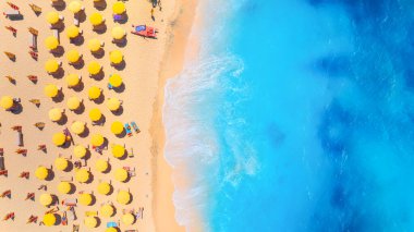 Yaz tatili ve dinlenme. Plaj, insanlar ve şemsiyeler. Kumsaldaki İHA 'nın ve gök mavisi denizin üst görüntüsü. İHA 'dan sahile bak. Arkaplan, duvar kağıdı, kartpostallar.