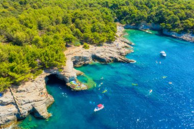 Sahilde kayalar ve ormanlarla dolu bir hava manzarası. Körfezde kayıklar ve kanolar. Tatil ve yaz tatilinde dinlenme. Kumsaldaki ve masmavi denizdeki İHA 'nın üst görüntüsü. 