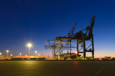 Denizci ticari terminali. Malların konteynırlarda taşınması. Kargo teslimatı için deniz taşımacılığı. Endüstri. Gün batımında vinçlerin siluetleri.