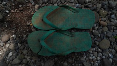 Yeşil parmak arası terlikler, yırtılmış ve kırılmış, yere saçılmış taşlarla