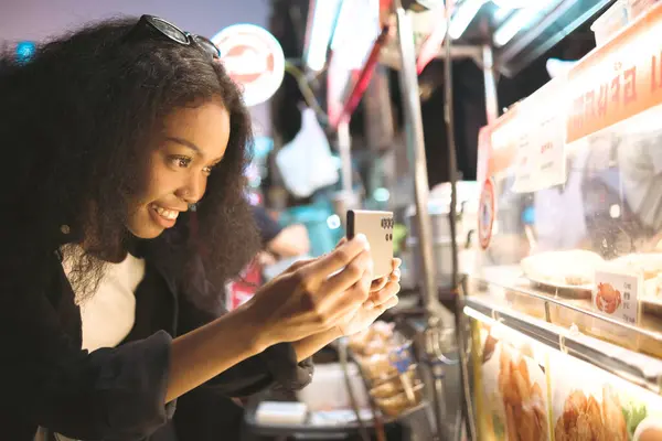 Asian woman enjoy travel in  downtown district and she taking a photo and using mobile live on social media and tasting streetfoods.