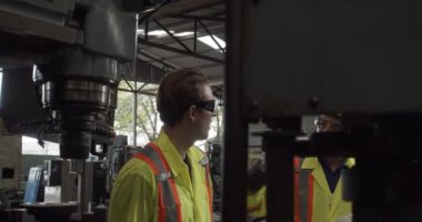 İşçi, fabrikada makineyle çalışmadan önce meslektaşına kask veriyor.