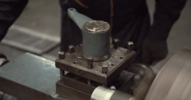 Makineler üzerinde çalışan genç bir mühendis kollarını kavuşturup kameraya bakıyor ve gülümsüyor..