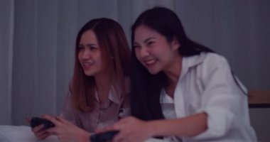Genç Asyalı kadın oda arkadaşı elinde joystickle geceleri yatakta oyun oynuyor.