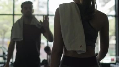 Bir kadın arkadaşını selamlar ve spor salonunda halter kaldırmaya gider..