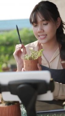 Bahçede kaktüs saksısı satmak için cep telefonu kullanan Asyalı kadın.