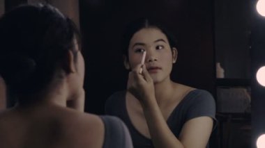 Aynanın önünde makyaj yapan genç bir kadın.