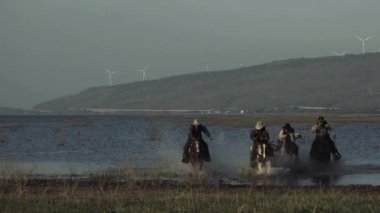 Tabancalı kovboylar gün batımında vahşi tarlada ata biniyorlar.