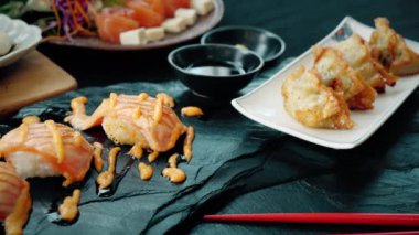 Japon yemeği, somon balığı, uskumru, tatlı soslu Japon pilavı ve siyah arka planda somon salatası..