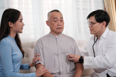 Doktor, Asyalı bir dedeye, kızına ve torununa evde sağlık kontrolü yapıyor.