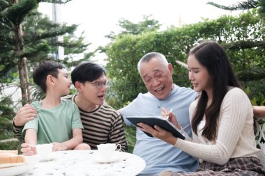 Mutlu Asyalı aile bahçede vakit geçirmeyi sever, büyükanne ve büyükbaba kızına tablet bakar ve oğluyla gülümserler..