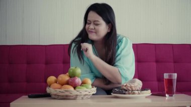 Şişman bir kadın, masada meyve ve çörek arasında seçim yapmaya karar verir..