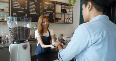 Müşteri kahve dükkanında sıcak içecek almak için e-ödemeyi cep telefonuyla yapıyor.