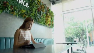 Barista, masada tabletle çalışan genç Asyalı kadına kahve servisi yapıyor..