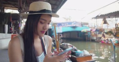 Genç Asyalı turist keyifli ve keyifli bir sokak yemeği ve gezisi ile Damnoen Saduak Yüzen Market Tayland kanalı boyunca tekne gezisi görüyor.