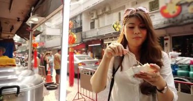 Genç Asyalı kadın turist gezgin ve Çin kenti Bangkok Tayland 'da sokak yemeği yiyor.