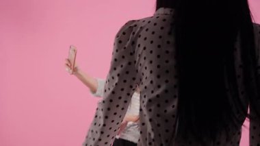 Güneş gözlüklü birkaç genç kız selfie çekiyor ve pembe arka planda gülümsüyor.