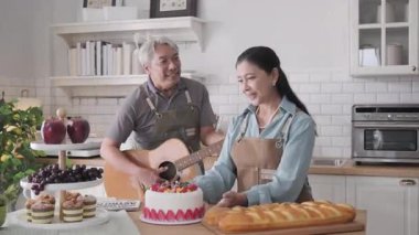 Mutlu son sınıf Asyalı çift evde gitar çalıp kek pişiriyor.
