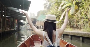 Genç Asyalı turist neşeli ve mutlu görünüyor Damnoen Saduak yüzen Market Tayland kanalı boyunca tekne ile seyahat görmek.