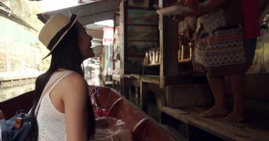 Genç Asyalı kadın turist fotoğraf çekip gülümsüyor Damnoen Saduak yüzen marketi Tayland kanalı boyunca tekneyle seyahat ediyor.