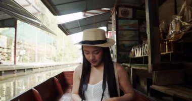 Genç Asyalı kadın turist fotoğraf çekip gülümsüyor Damnoen Saduak yüzen marketi Tayland kanalı boyunca tekneyle seyahat ediyor.