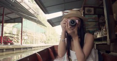 Genç Asyalı kadın turist fotoğraf çekip gülümsüyor Damnoen Saduak yüzen marketi Tayland kanalı boyunca tekneyle seyahat ediyor.
