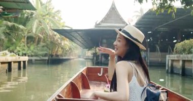 Genç Asyalı kadın turist fotoğraf çekip gülümsüyor Damnoen Saduak yüzen marketi Tayland kanalı boyunca tekneyle seyahat ediyor.