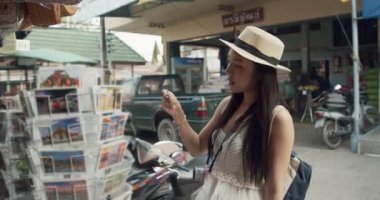 Genç Asyalı bayan turist kartpostal seçiyor ve gülümsüyor.