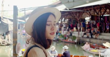 Genç Asyalı bayan turist kameraya bakar ve gülümser. Damnoen Saduak yüzen marketi Tayland kanalı boyunca tekneyle seyahat eder.