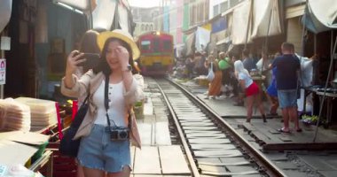 Maeklong Tren İstasyonu (Talad Rom Hub) Tayland 'da cep telefonuyla selfie çeken genç Asyalı kadın turist..