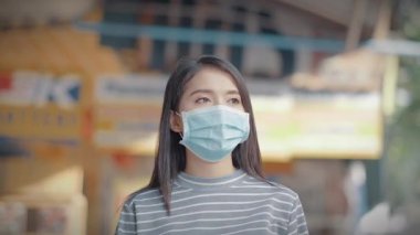 Genç Asyalı kadın gülümsemesi ve yüz maskesi takıp sokakta yürüyor.