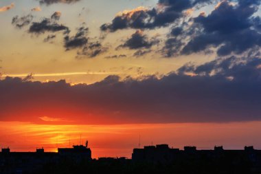 Gün batımında bulutlarla kaplı gökyüzü şehrin çatılarının gölgelerine karşı..