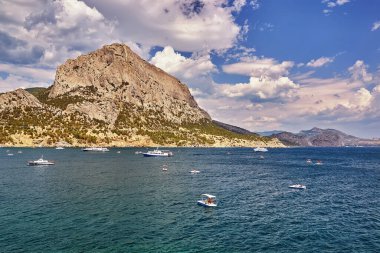 Yaz manzarası - kayalık deniz kıyısı ve güneşli bir günde turistlerle dolu tekneler. Yukarıdan görüntüle.