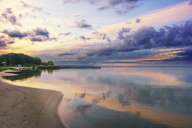 Gün batımında fırtına bulutları olan bir orman gölünün kumlu kıyısı..