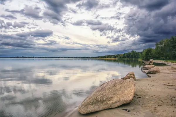 stock image Sandy shore of a forest lake with storm clouds at sunset.