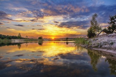 Gölün üzerinde gün batımı. Bulutlu gökyüzü suya yansıyor.