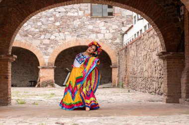 Frida 'dan esinlenerek Frida Kahlo' yu andıran Meksikalı bir kadın narin kemer yolları altında yaşlanmış bir sandalyeyi şereflendirir. Bir ışık ve gölge oyunuyla yıkandı, geleneksel kıyafetleri ve derin derin bakışları