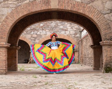 Frida 'dan esinlenerek Frida Kahlo' yu andıran Meksikalı bir kadın narin kemer yolları altında yaşlanmış bir sandalyeyi şereflendirir. Bir ışık ve gölge oyunuyla yıkandı, geleneksel kıyafetleri ve derin derin bakışları
